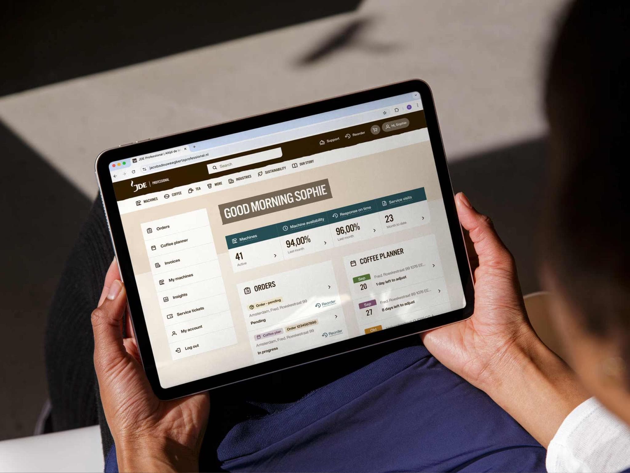 Two hands holding an iPad in landscape mode showing a dashboard